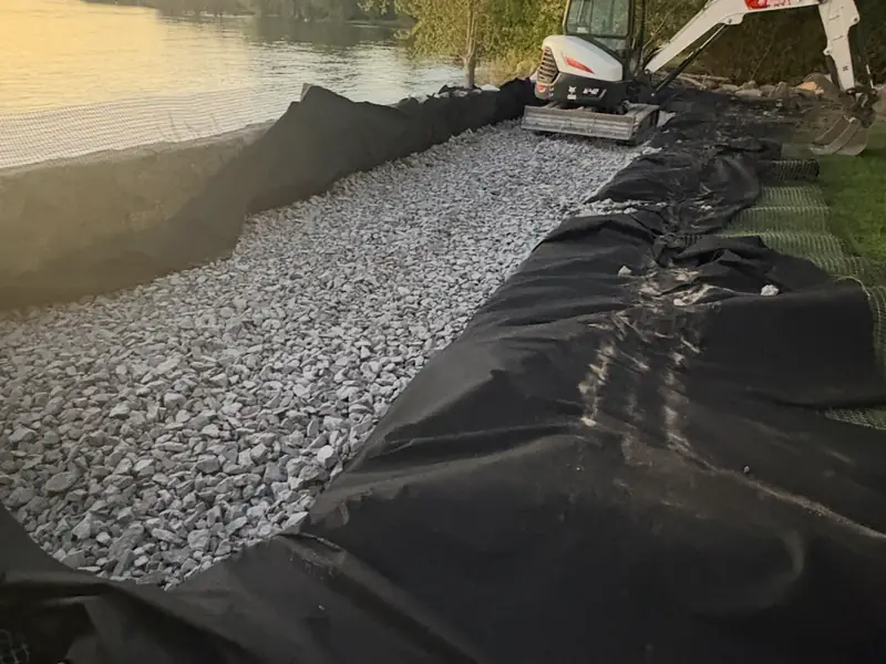 Géotextile et gravier étendus au bord de l'eau en fin de journée, chantier de l'Entreprise SME