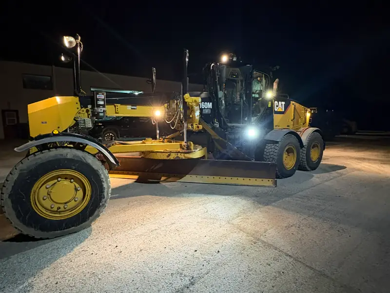 Niveleuse de l'Entreprise SME au travail de nuit, phares allumés dans la neige